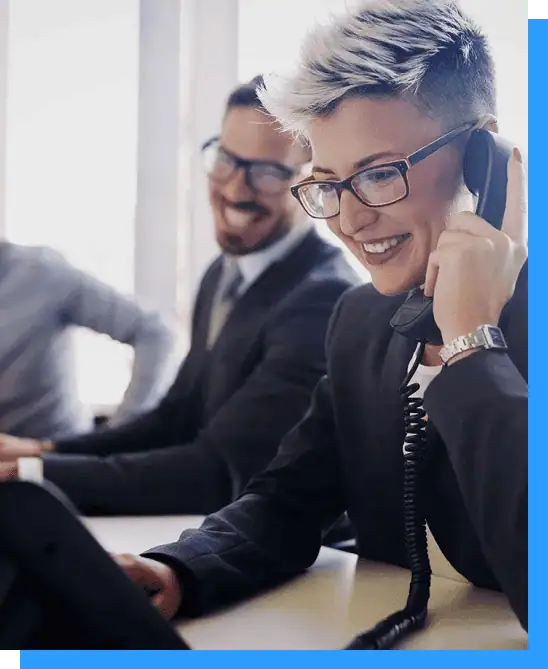 Businesswoman wearing glasses, talking on the phone at her desk in a professional office environment.