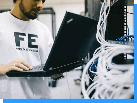 Laptop technician working on network cables and server racks in a data center or IT infrastructure environment at Rivell.