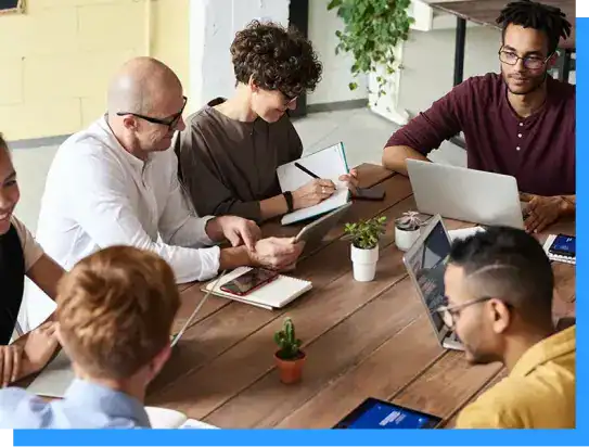 Group of diverse professionals collaborating around a table in a modern office environment, engaging in a business meeting or team discussion.