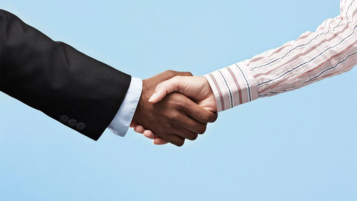 Partnership handshake between a businessman in a black suit and a professional in a striped shirt, symbolizing collaboration, trust, and business success.